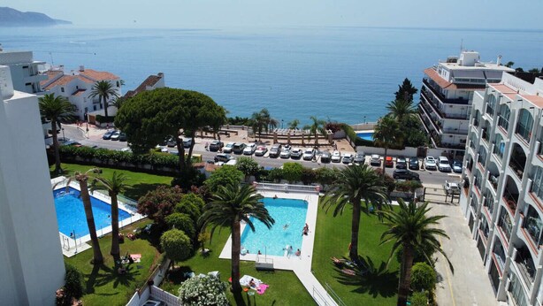 A view of a hotel with a swimming pool, palm trees, and a view of the sea.