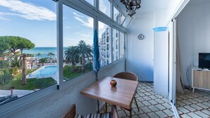 A balcony with a wooden table, wicker chairs, a view of a pool and palm trees, and a hanging lamp.