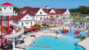 A swimming pool area with a water slide, lounge chairs, and a building with a red roof. - Coastal Club * 6 BR Twin Lewes Beach Home rentals (Lewes)