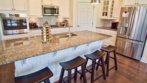 A kitchen with white cabinets, stainless steel appliances, a granite countertop, and bar stools. - Coastal Club * 6 BR Twin Lewes Beach Home rentals (Lewes)