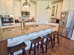 A kitchen with white cabinets, stainless steel appliances, a granite countertop, and bar stools.