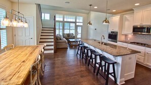 A kitchen with a wooden dining table, bar stools, a staircase, and a large window. - Coastal Club * 6 BR Twin Lewes Beach Home rentals (Lewes)