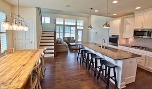 A kitchen with a wooden dining table, bar stools, a staircase, and a large window.