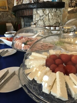 A buffet table with various food items covered by glass domes, including cheese, tomatoes, and other prepared foods.