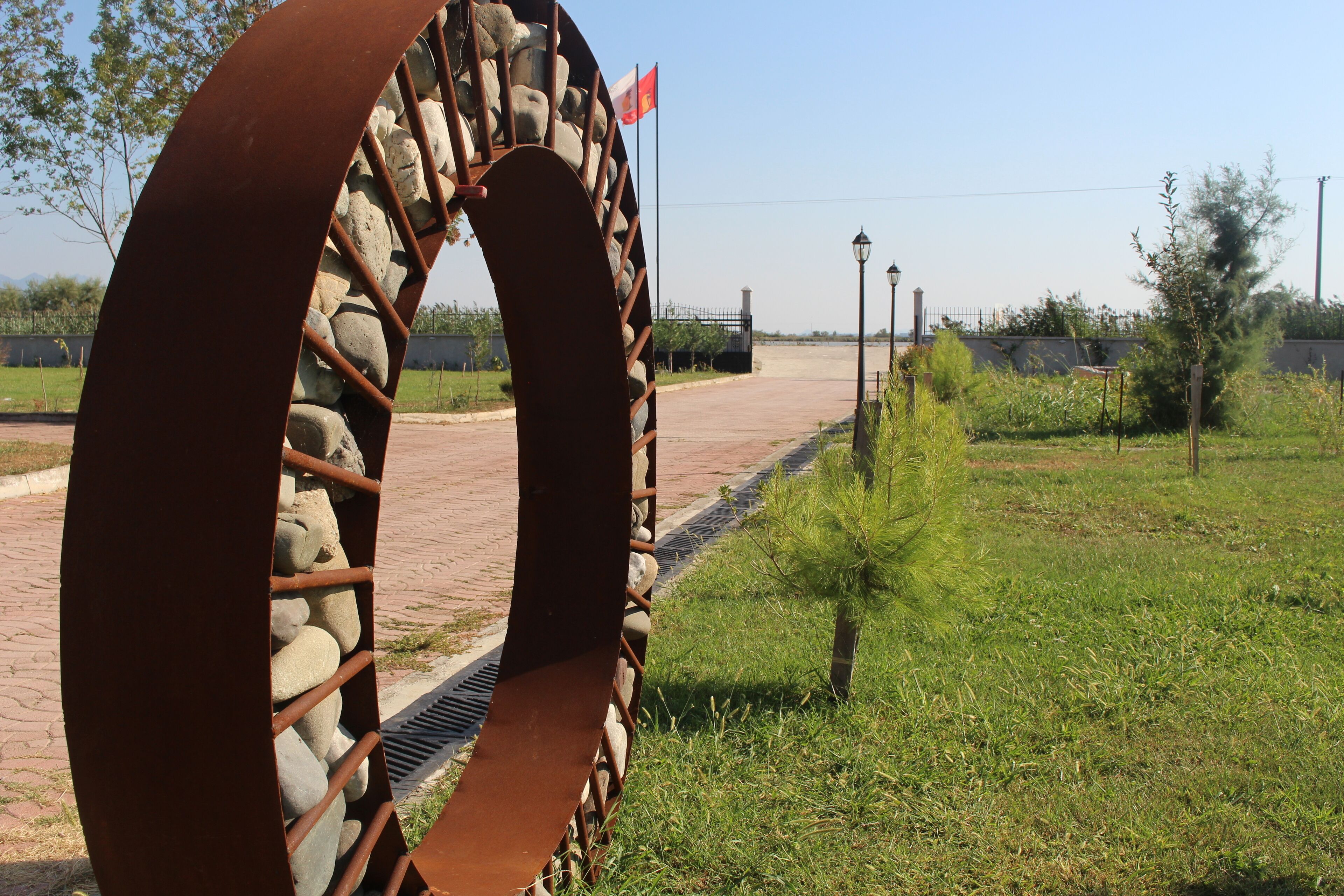 A large metal archway with a flag, surrounded by greenery and a paved path.