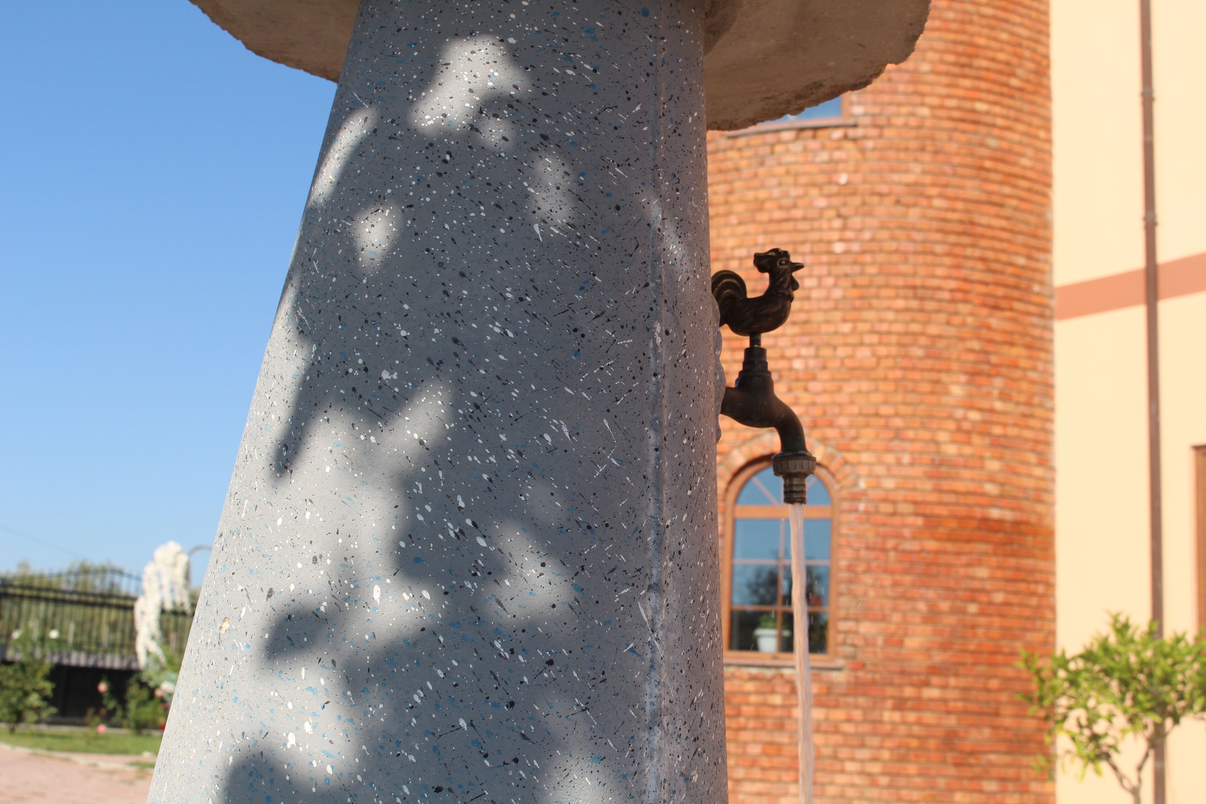 A stone column with a rooster statue attached to it, set against a brick building with a window.