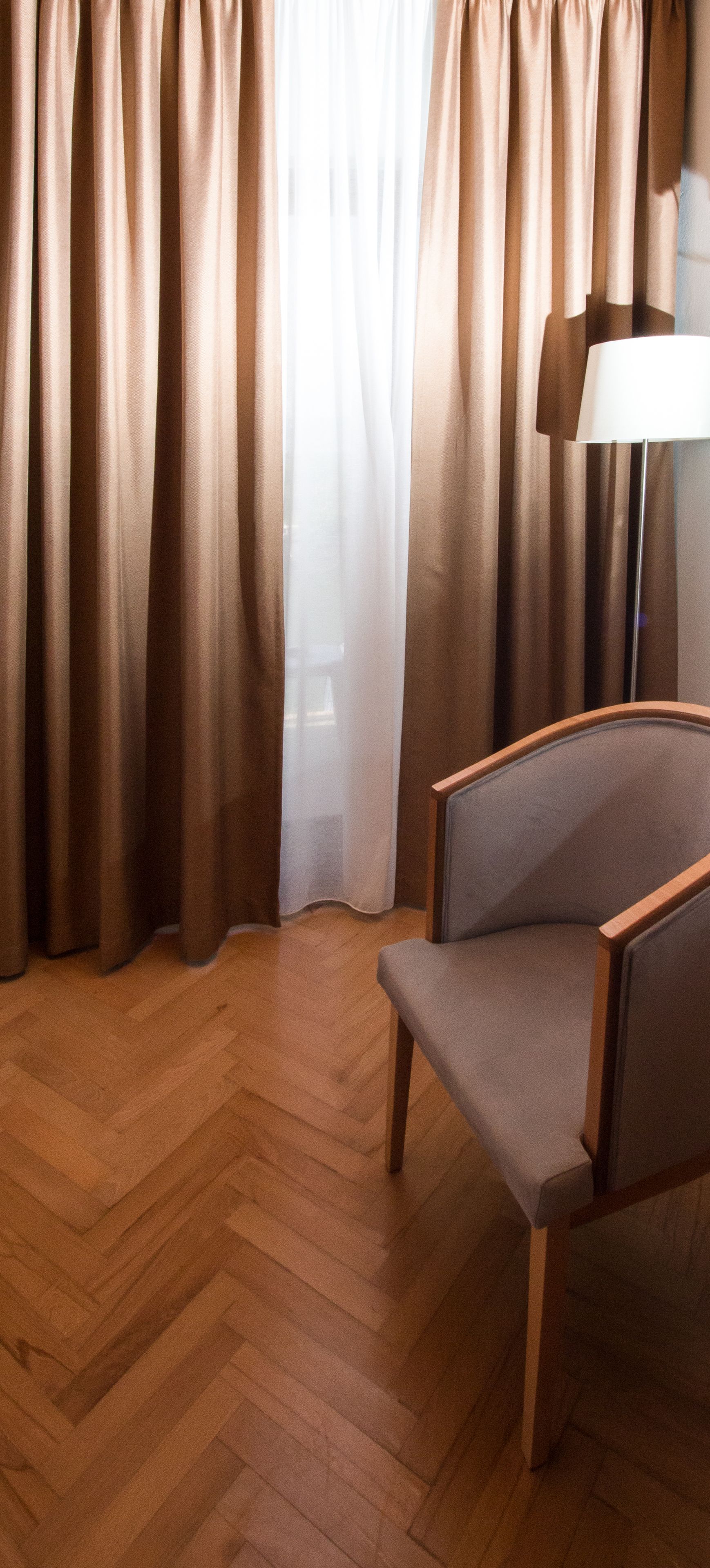 A room with a wooden herringbone floor, a grey upholstered armchair, and a lamp on a table.