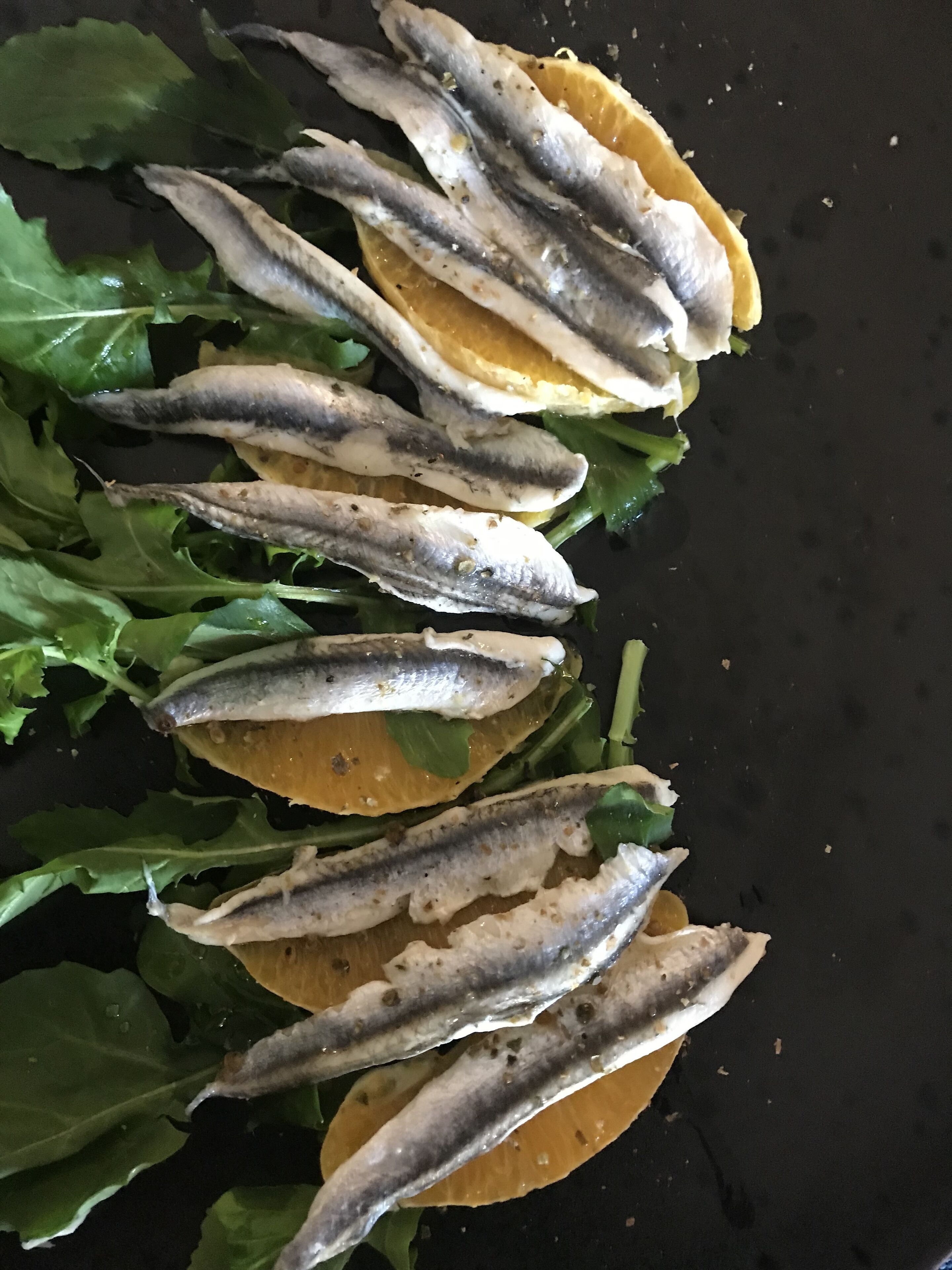 A close-up of a dish with fish and lemon slices on a bed of greens.