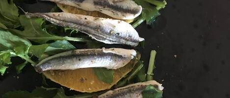 A close-up of a dish with fish and lemon slices on a bed of greens.