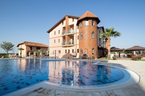 A swimming pool with a brick tower and a multi-story building with balconies.