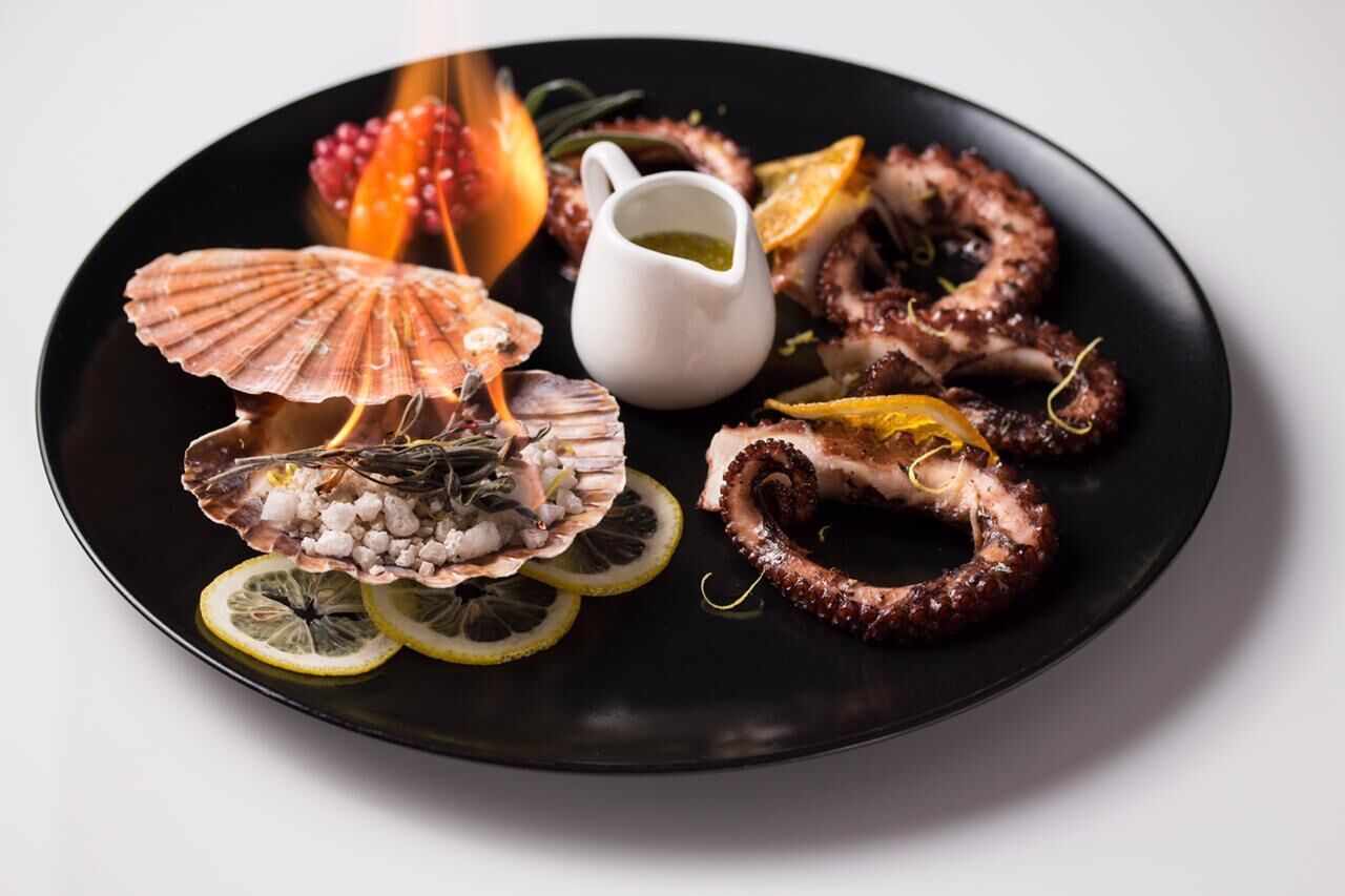 Ein Teller mit Meeresfrüchten, darunter Jakobsmuscheln, Oktopus und Zitronenscheiben.