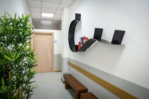 A hallway with a wooden door, a plant, and a wall-mounted shelf with books and a speaker.