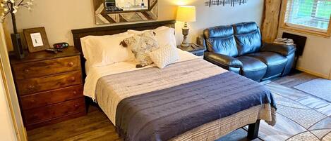 A bedroom with a bed, a dresser, a chair, a lamp, and a wall-mounted mirror.