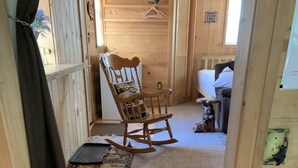 Ein Holzinnenraum mit Schaukelstuhl, Bett und kleiner Teppich.
