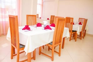 A dining area with round tables, wooden chairs, and white tablecloths. - Ambiere House (Mtwara)