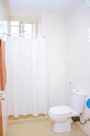 A bathroom with a toilet, a shower curtain, and a towel rack. - Ambiere House (Mtwara)