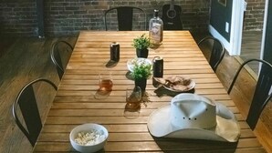 Una mesa de madera con sillas, un cuenco de galletas, una jarra de cerveza, una botella de licor, una pequeña planta y un sombrero de vaquero.