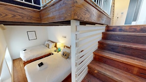 Una habitación con dos camas, una escalera de madera y una barandilla blanca.