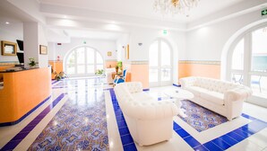 A lobby with a reception desk, two white sofas, patterned floor tiles, and a chandelier. - Odysseus Hotel (Lipari)