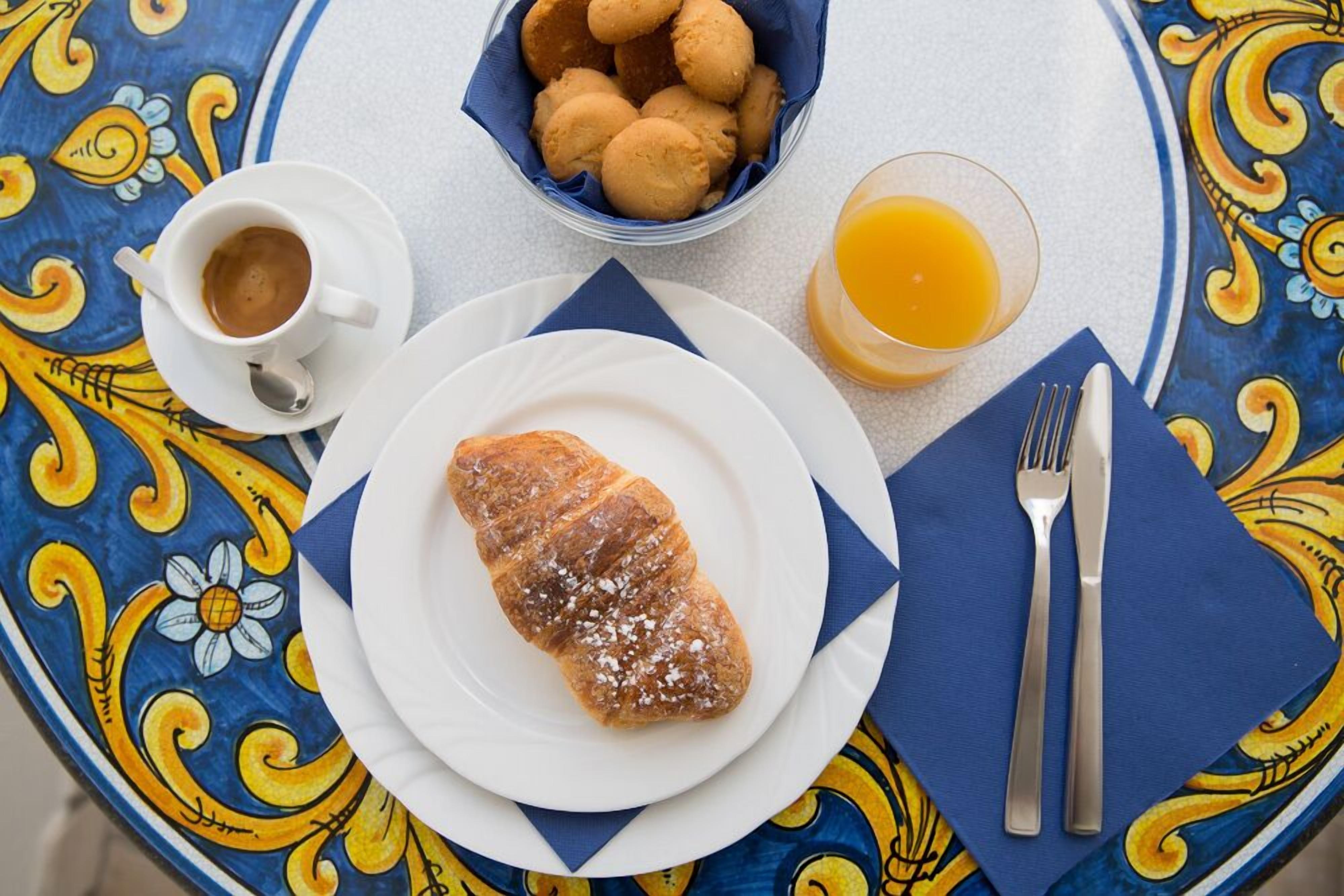A table with a croissant, a cup of coffee, a glass of orange juice, and a bowl of cookies.