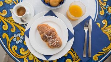 A table with a croissant, a cup of coffee, a glass of orange juice, and a bowl of cookies.
