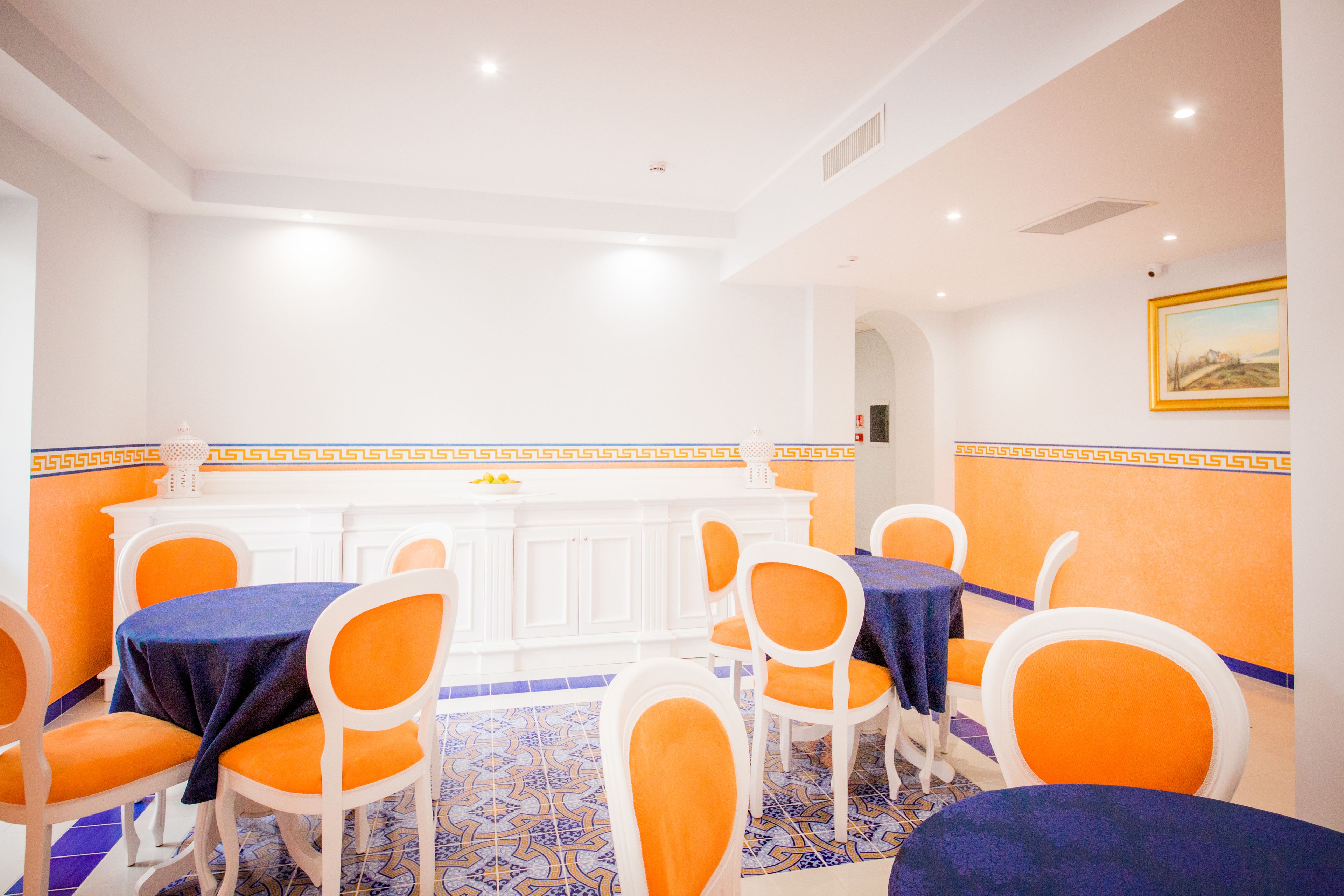 Un comedor con sillas y mesas blancas, una barra blanca y baldosas de suelo estampadas.