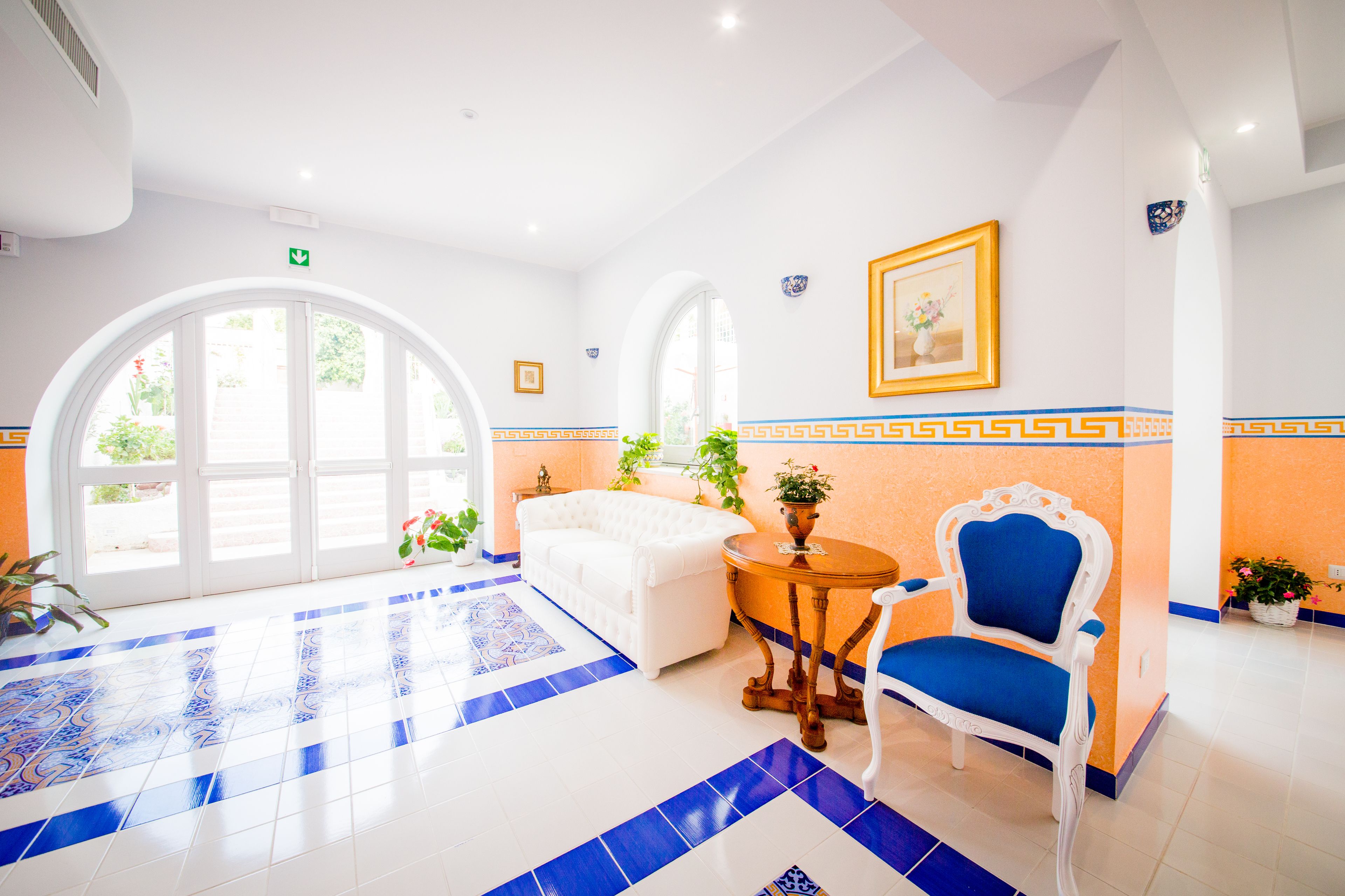 A hotel lobby with a white sofa, a blue chair, a round table, and a large arched window.