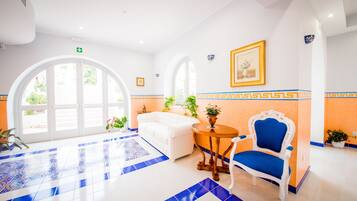 A hotel lobby with a white sofa, a blue chair, a round table, and a large arched window.