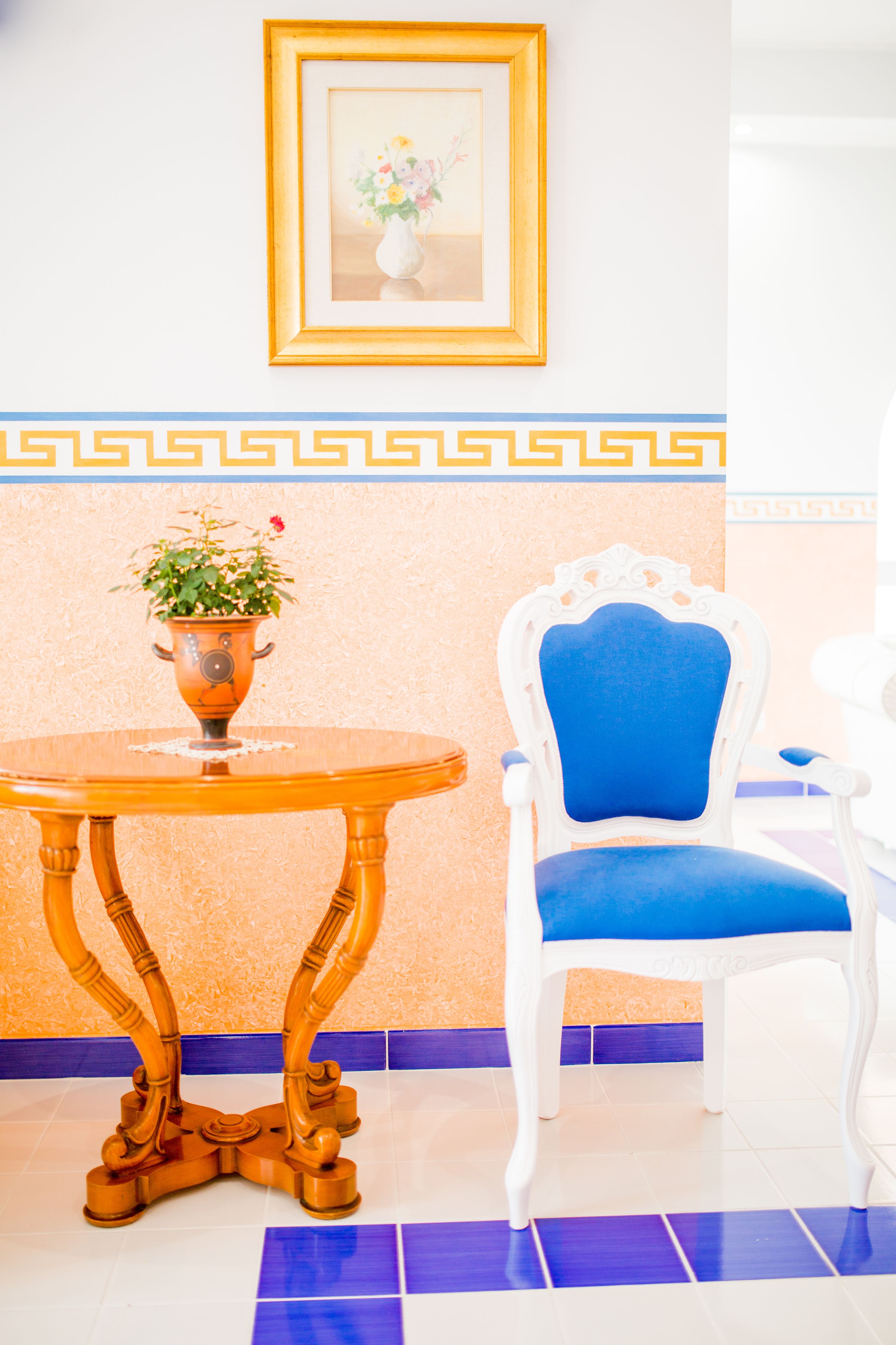 Una habitación con una mesa redonda de madera, una planta en maceta, una silla azul y un cuadro en la pared.