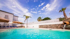 A swimming pool with clear blue water, lounge chairs, and palm trees. - Odysseus Hotel (Lipari)