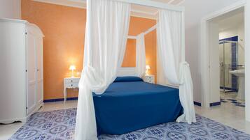 A bedroom with a four-poster bed, a nightstand with a lamp, and a wardrobe.
