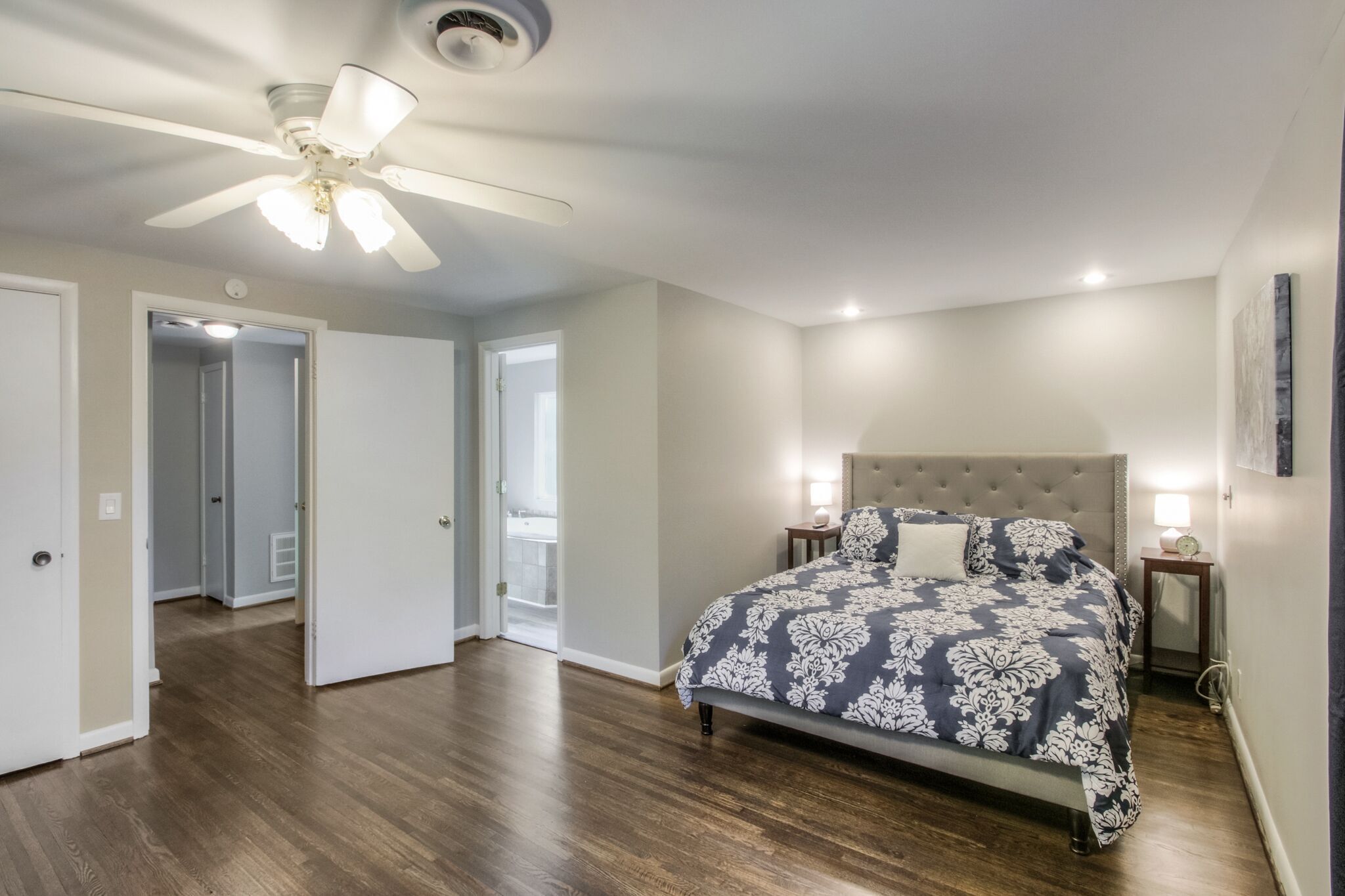 A bedroom with a bed, a ceiling fan, and a nightstand with a lamp.