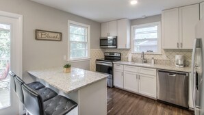 A modern kitchen with white cabinets, a granite countertop, stainless steel appliances, and a bar area with black leather chairs. - Vintage Charm-Wine cellar/bar room, sleeps 12! (Nashville)
