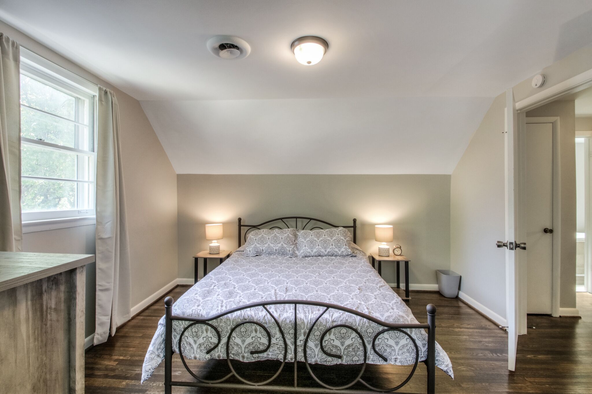 Un dormitorio con cama, dos lámparas de noche, una ventana con cortinas y una puerta.
