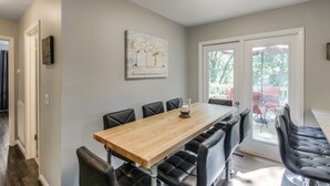 A dining area with a long wooden table and black upholstered chairs, a painting on the wall, and a view through a glass door to the outside. - Vintage Charm-Wine cellar/bar room, sleeps 12! (Nashville)