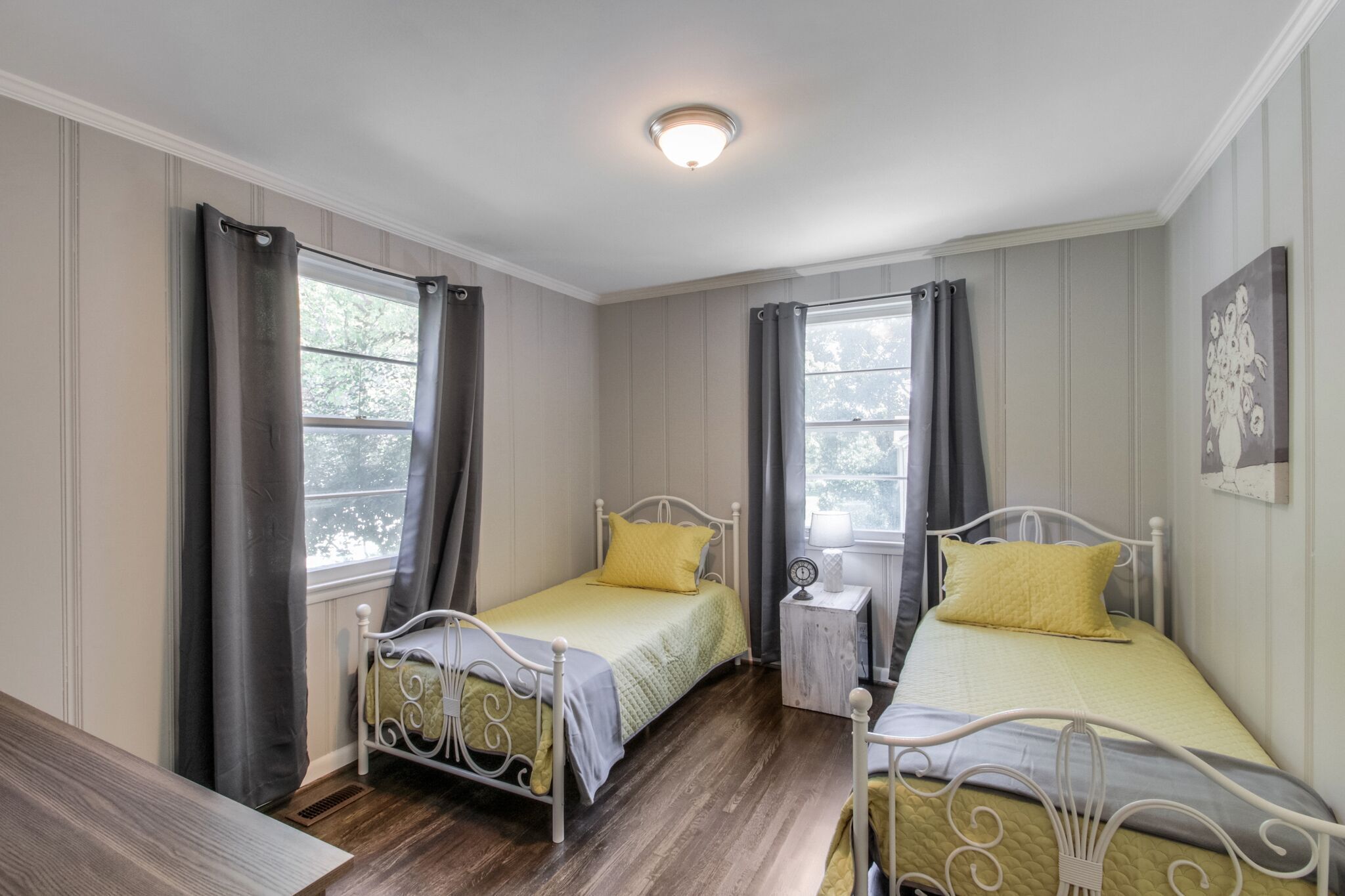 Quarto com duas camas, uma mesinha de cabeceira com abajur e uma janela com cortinas.