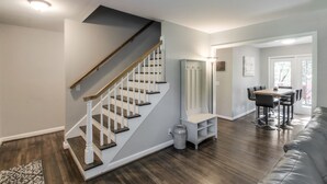 A modern living room with a wooden staircase, a dining area, and a large window. - Vintage Charm-Wine cellar/bar room, sleeps 12! (Nashville)