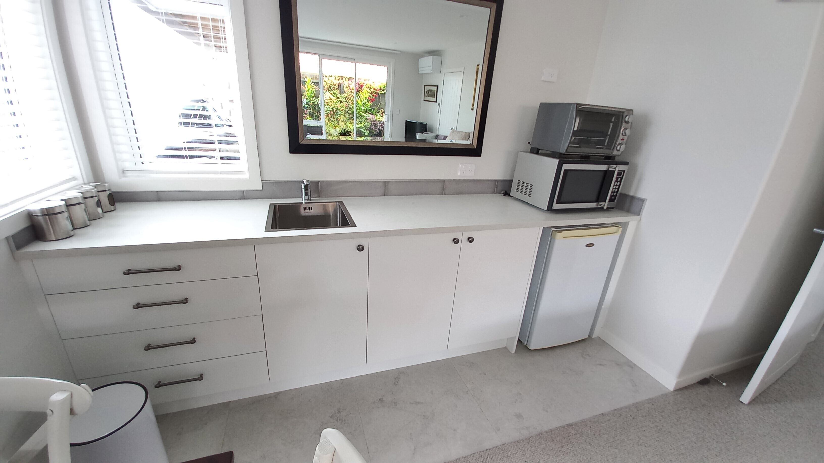 Een moderne keuken met witte kastjes, een roestvrijstalen spoelbak, een magnetron en een compacte koelkast.