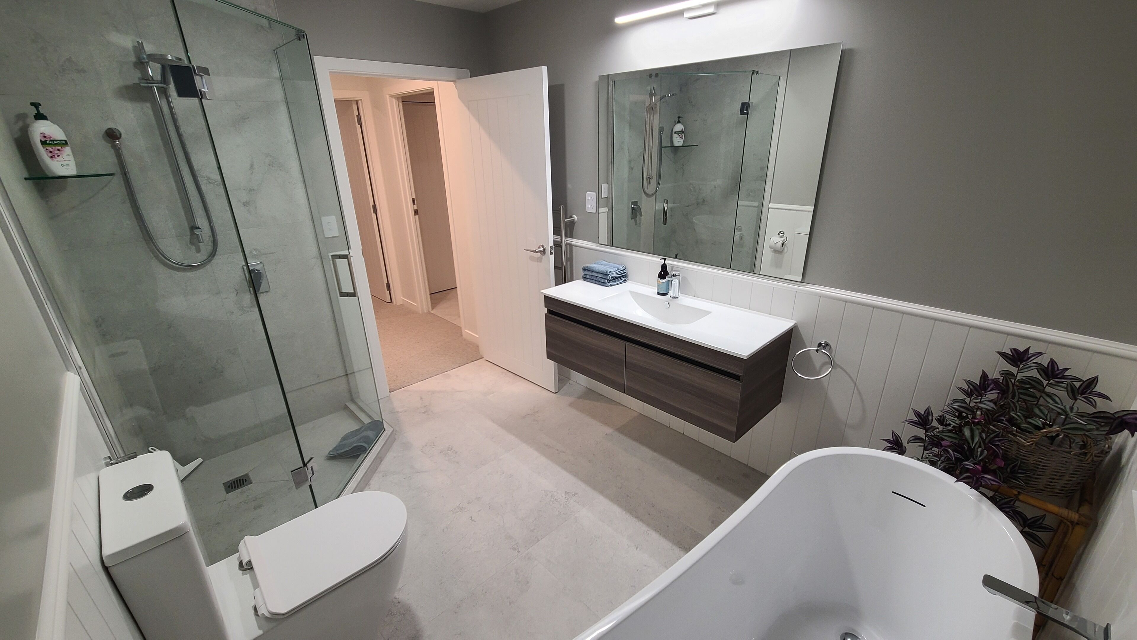 Un baño moderno con ducha envuelta en vidrio, una bañera blanca y un tocador con espejo.