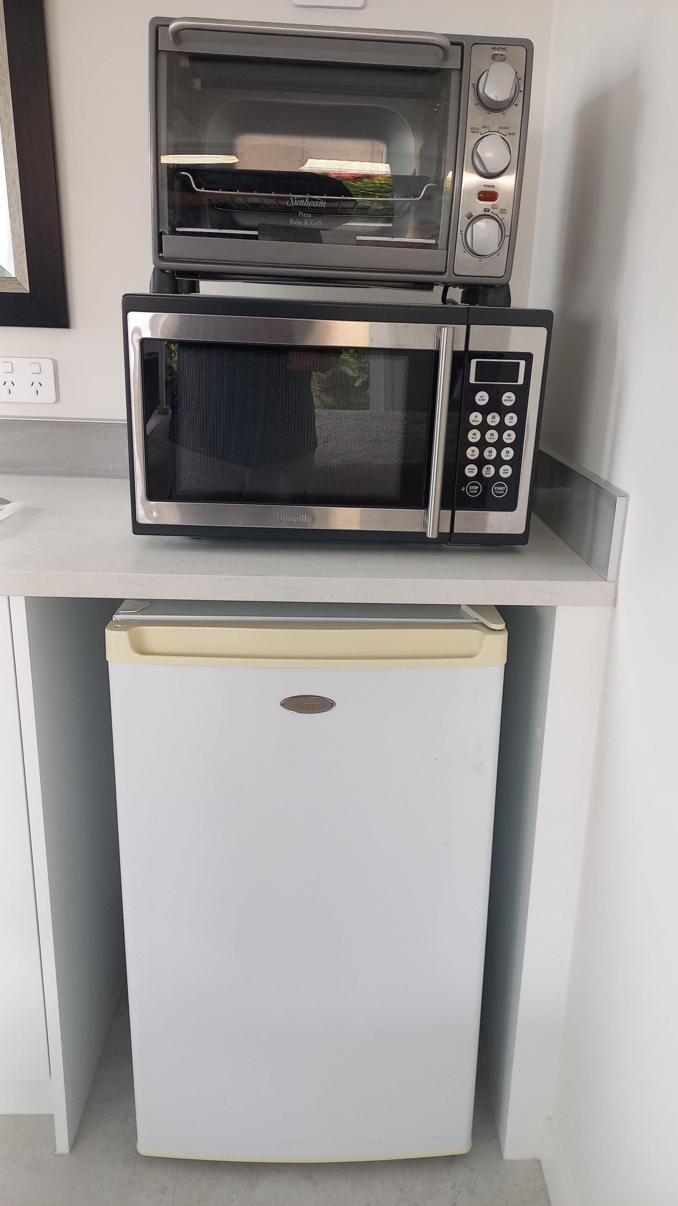 A compact kitchen with a built-in microwave and toaster oven on a white countertop.