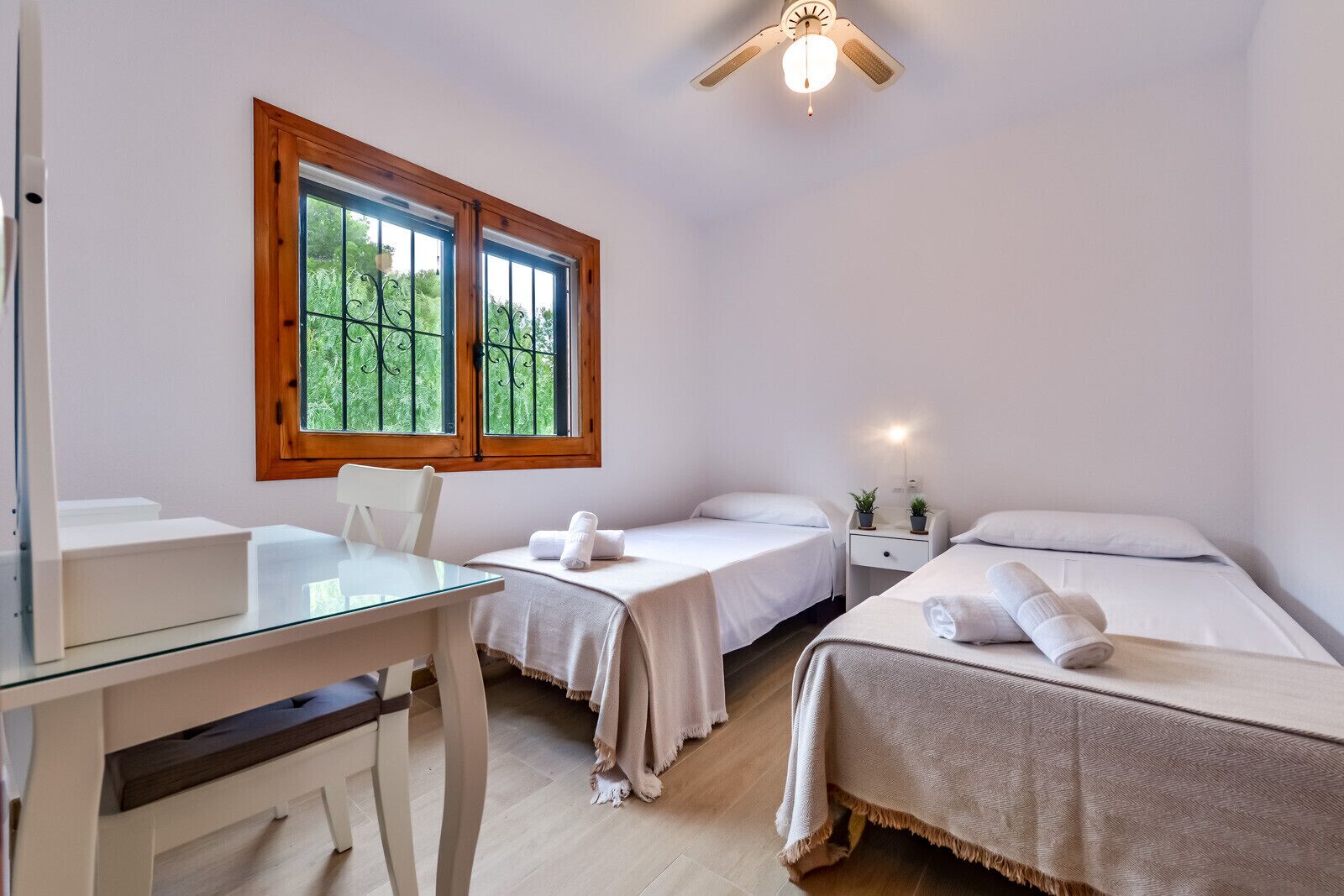 Een slaapkamer met twee bedden, een bureau en een raam met uitzicht op groen.