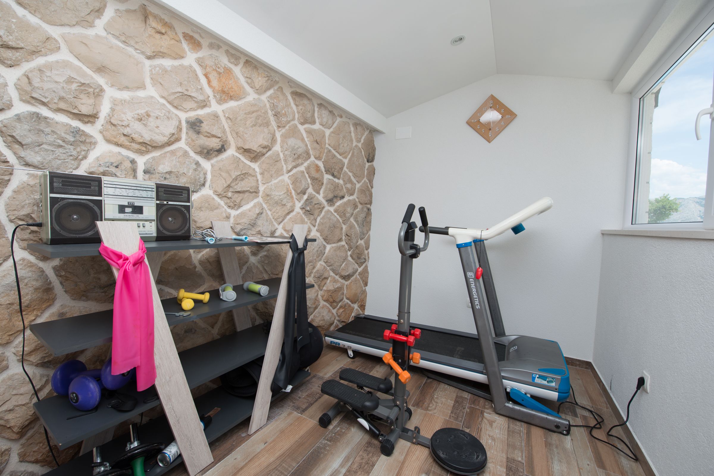 Ein Heimfitnessraum mit Steinwand, Laufband, Kurzhanteln und Radio.