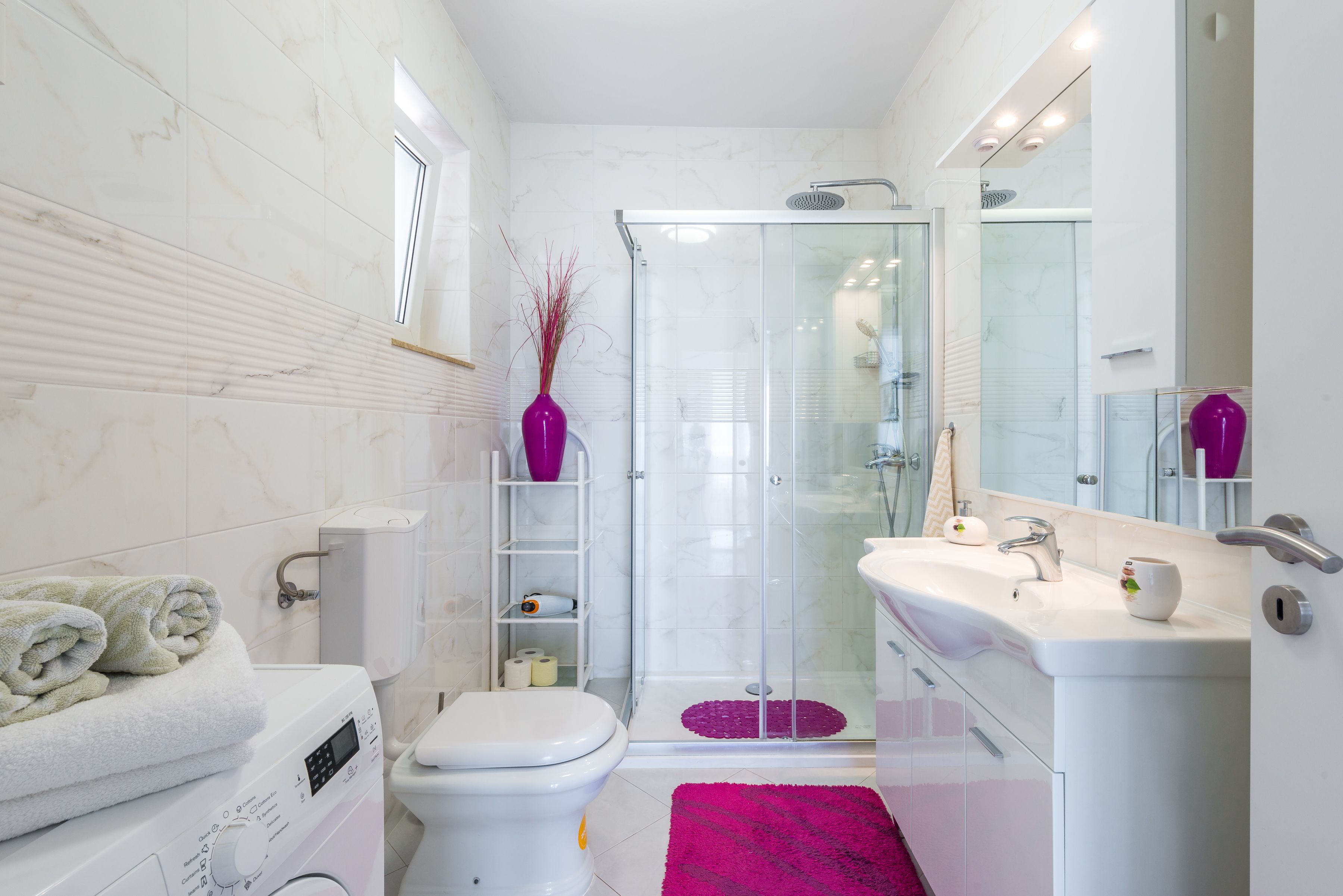 Un baño moderno con cabina de ducha de vidrio, inodoro blanco, lavadora y lavabo con espejo.