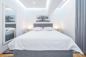 A modern bedroom with a large bed, a ceiling light, a wall-mounted artwork, and a nightstand with a lamp. - Villa Markoc (Konavle)