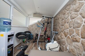 A small gym with exercise equipment, a water dispenser, and a stone wall.