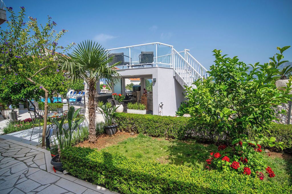 Un espacio exterior moderno con una zona de estar cubierta de cristal, una piscina y abundante vegetación.