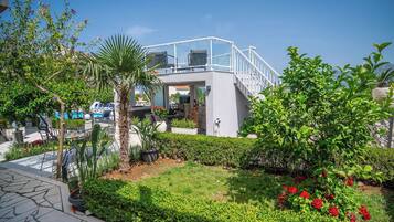 Un espacio exterior moderno con una zona de estar cubierta de cristal, una piscina y abundante vegetación.