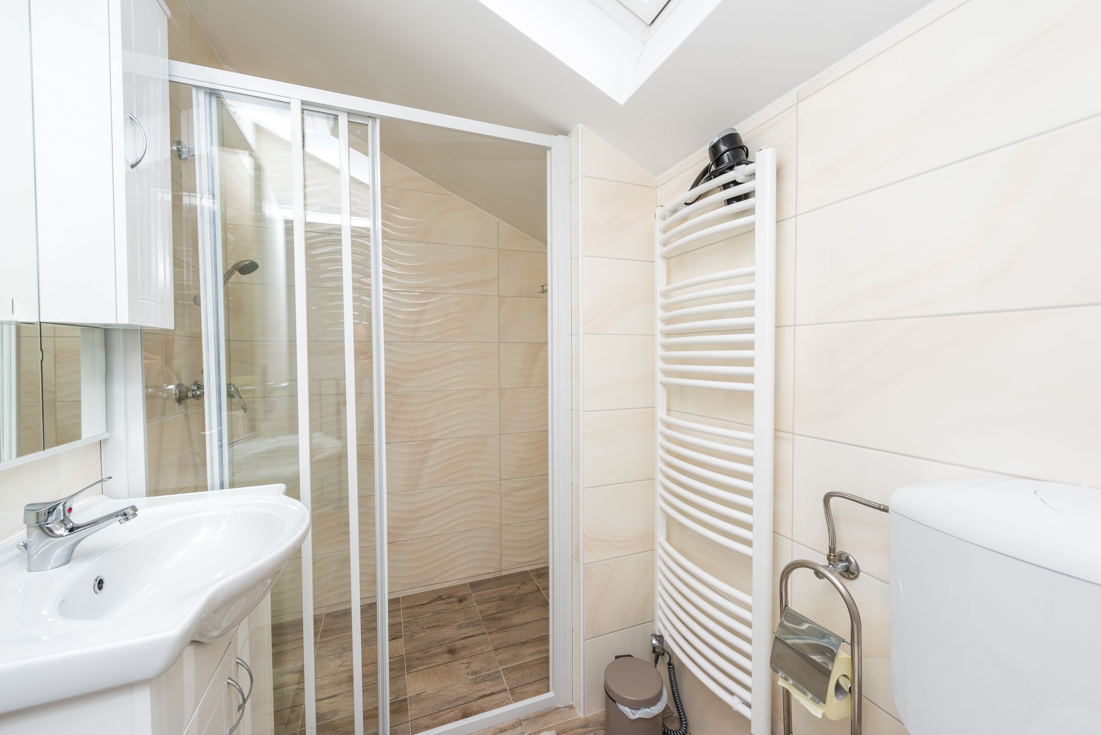 A bathroom with a glass shower enclosure, a white sink, a toilet, and a towel rack.