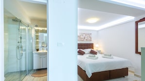 Een moderne slaapkamer met een groot bed, een douchecabine van glas en een witte badkamer.