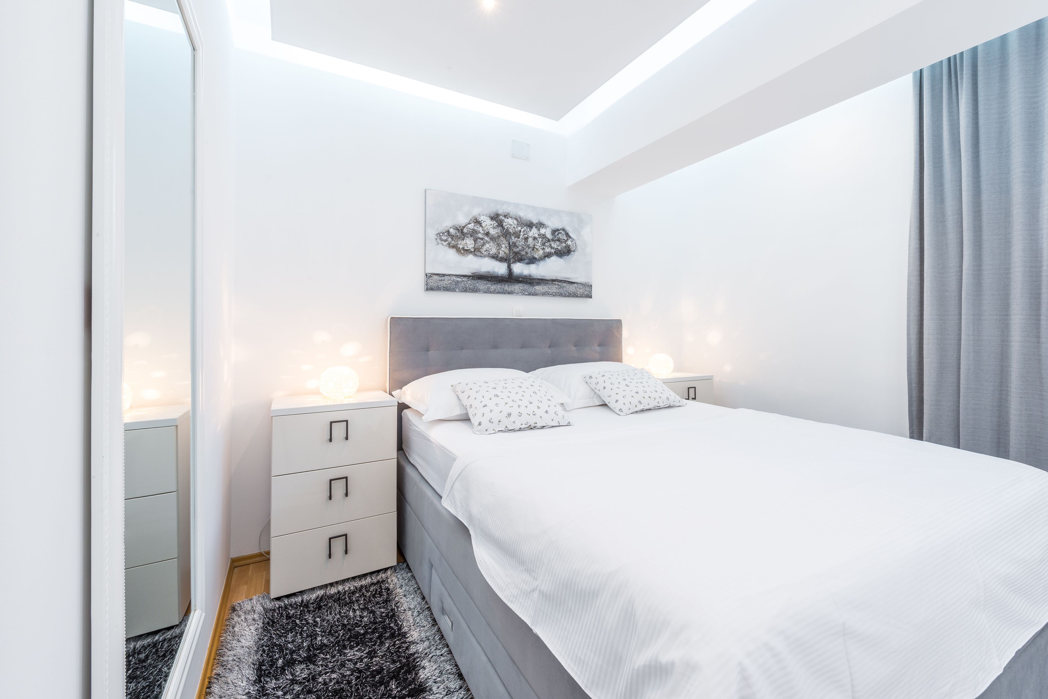 Een moderne slaapkamer met een groot bed, nachtkastjes, een hanglamp en een schilderij aan de muur.